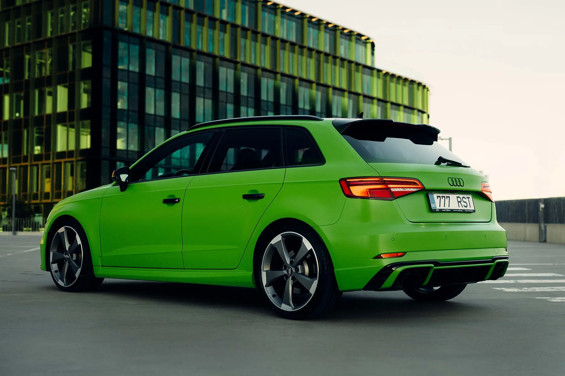 Roheline Audi RS3 tagantvaates klaasfassaadiga büroohoone ees