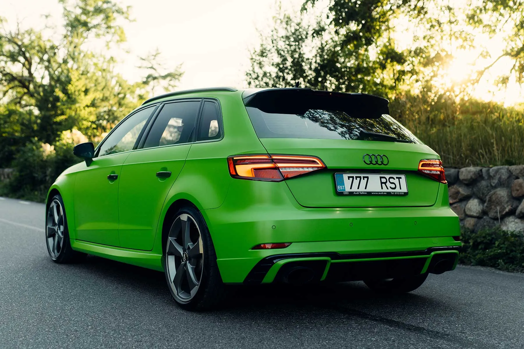 Roheline Audi RS3 tagantvaates puude vahel loojuva päikese valguses