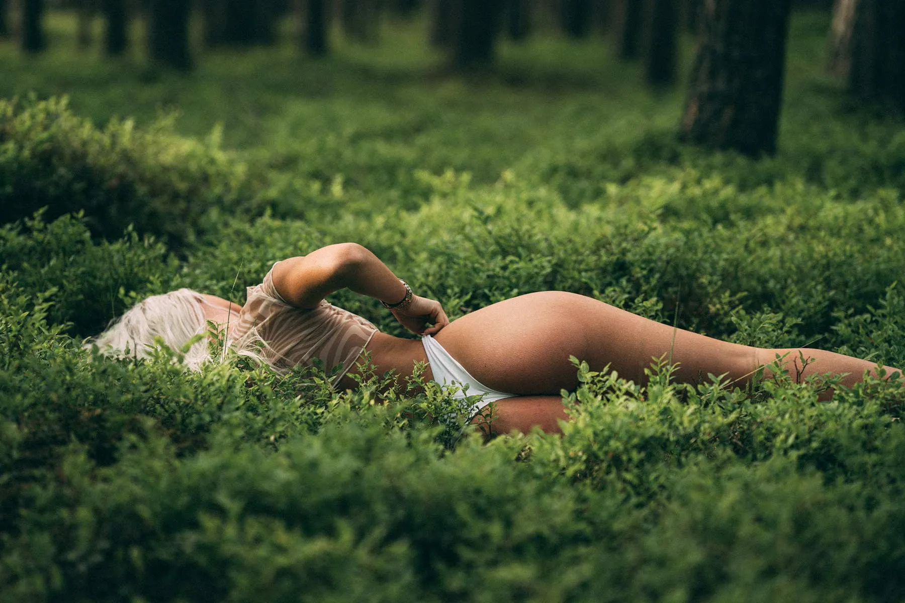 Buduaarifoto looduses: naine lebab mustikavarte vahel metsa all