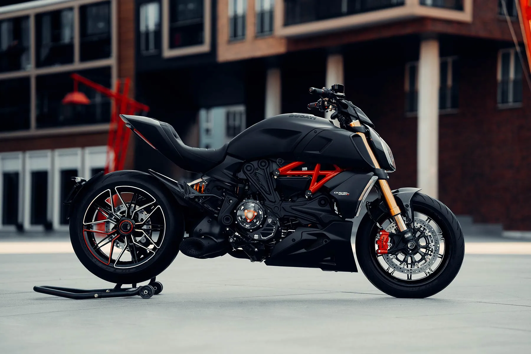 Must Ducati Diavel küljelt, taga tellismaja ja oranž terasskulptuur